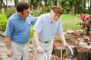 Senior man struggling to us a walker.  His adult son is helping him.